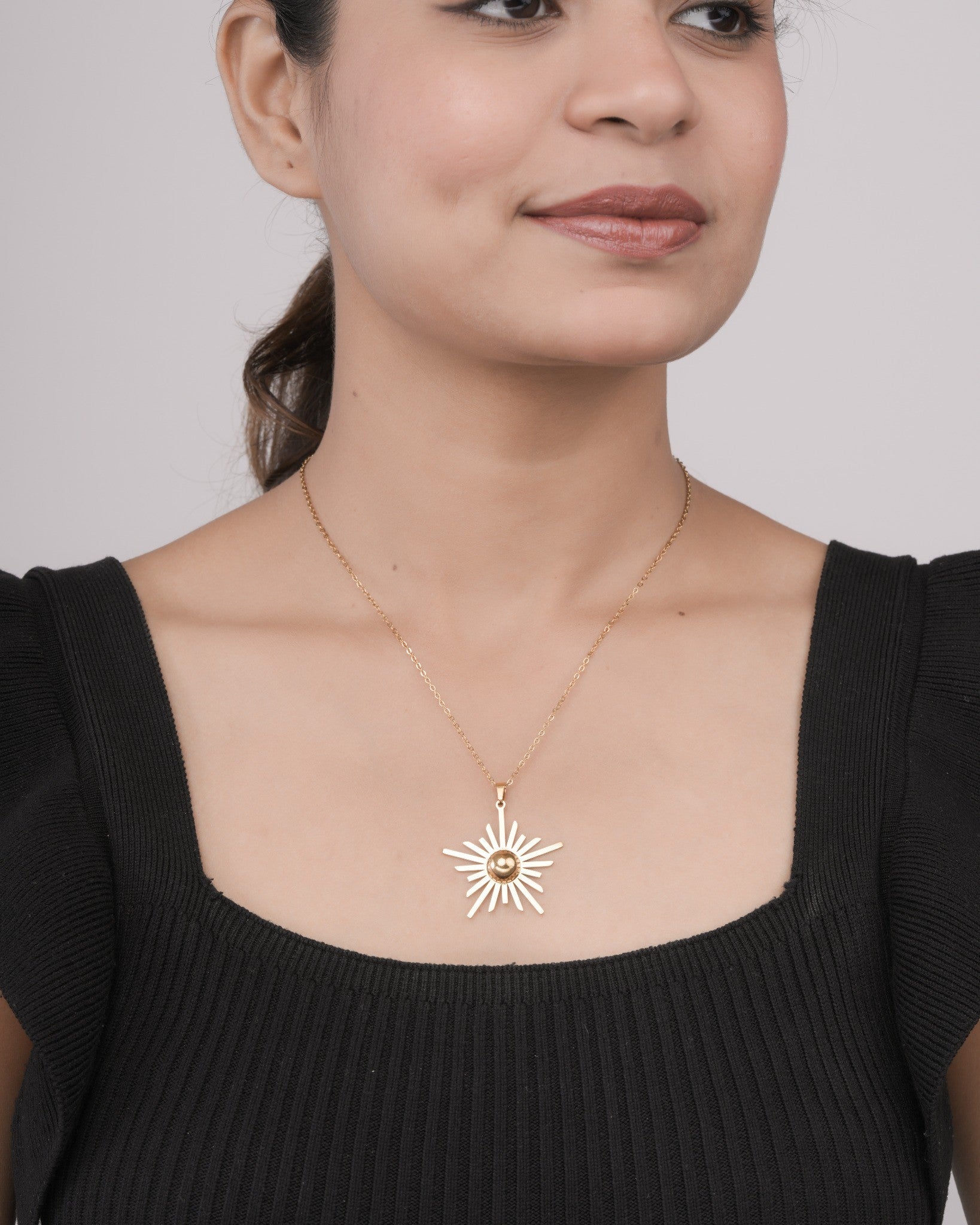 Woman wearing gold sunburst pendant necklace on delicate chain with black square neckline top